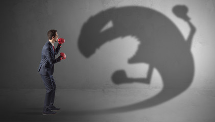 Businessman with boxing glove fighting with a big monster shadow
