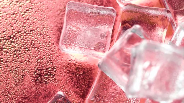Crystal ice cubes rotating on rose gold surface with water drops. Close up macro 4k footage.