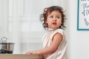 Little beautiful girl in powdery dress sits behind straw in the kitchen and looks away, close-up, indoors