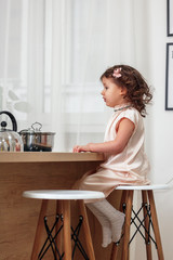 Little beautiful girl in powdery dress sits behind straw in the kitchen and looks away, close-up, indoors