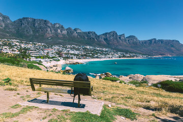 Backpack of lonely traveller on a bench with a view of Camps bay beautiful beach in Cape Town, South Africa