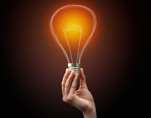 Hand holding light bulb on dark background. New idea concept