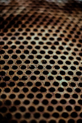 Perforated brown rusty iron sheet texture. Surface with depth of field, abstract industrial mesh. Vertical background