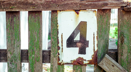White Shabby And Rusty Metal Plate With Black Nuber Four, Nailed On Green Old Fence