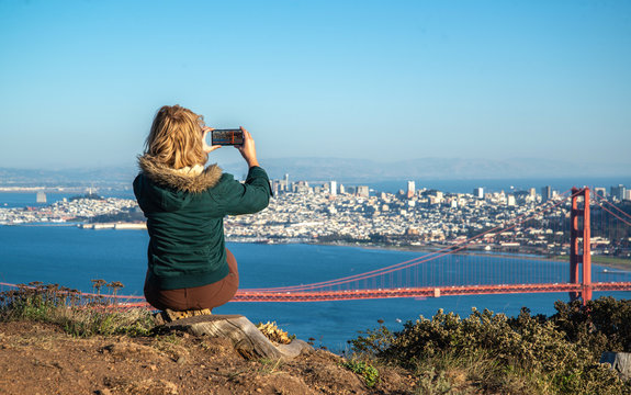 Young woman taking a photo with her phone of Golden Gate Bridge