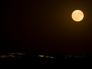 Fototapeta na wymiar Big full moon shining over coastal resort in complete darkness.