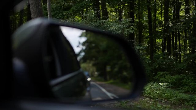 View out the rearview mirror as car drives on country road. 4K
