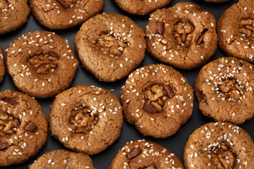 Pattern of oatmeal cookies with dried berries and sesame. View from above. On a black background.
