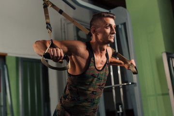 Young fit man doing TRX suspension chest exercises in the gym