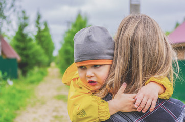 Mom carries a tired upset little son in her arms