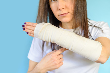 Middle aged woman with broken arm bone in cast, plastered hand on blue background. Selective focus on broken hand.