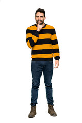 Full-length shot of Handsome man with striped sweater showing a sign of silence gesture putting finger in mouth on isolated white background