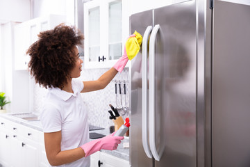 Young Woman Cleaning Refrigerator With Napkin