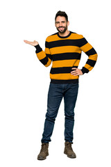 Naklejka premium Full-length shot of Handsome man with striped sweater holding copyspace imaginary on the palm to insert an ad on isolated white background