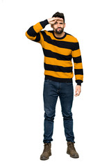 Full-length shot of Handsome man with striped sweater looking far away with hand to look something on isolated white background