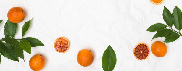 many fresh blood oranges and green leaves on white crumpled paper background