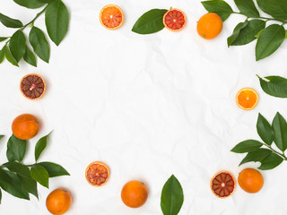 many fresh blood oranges and green leaves on white crumpled paper background