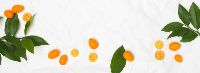 many fresh kumquats and green leaves on white crumpled paper background