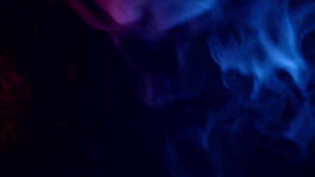 red and blue smoke patterns moving moving against at dark background 