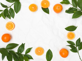 many fresh oranges and green leaves on white crumpled paper background