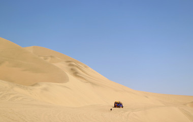 Fototapeta na wymiar Running dune buggy chasing by a naughty dog on the sand dunes of Huacachina desert, Ica region, Peru 