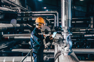Portrait of young Caucasian man dressed in work wear using tablet while standing in heating plant.
