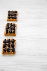 Vegetarian toasts with peanut butter, olives and chia seeds on a white wooden table, side view. Healthy dieting. Copy space.