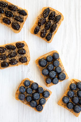 Vegan toasts with peanut butter, blueberries, olives and chia seeds on a white wooden background, top view. Healthy eating. Flat lay, from above.
