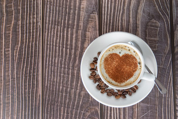 Obraz na płótnie Canvas Cup of coffee on a wooden table, with cocoa powder forming a heart on the foam