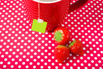 red mug with teabag and three strawberries over red background with copy space like fruit tea concept 