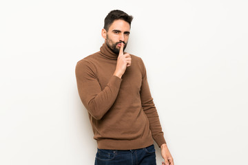 Handsome man over white wall showing a sign of silence gesture putting finger in mouth