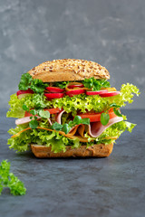 Big sandwich with ham, cheese and fresh vegetables on a dark board. Breakfast concept.