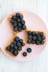 Vegan toasts with peanut butter, blueberries and chia seeds on a pink plate over white wooden surface, top view. Flat lay, overhead.
