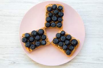 Vegan toasts with peanut butter, blueberries and chia seeds on a pink plate over white wooden background, top view. Flat lay, overhead.