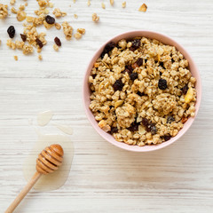 Pink bowl of fruit granola and honey on a white wooden background, top view. Overhead, from above.