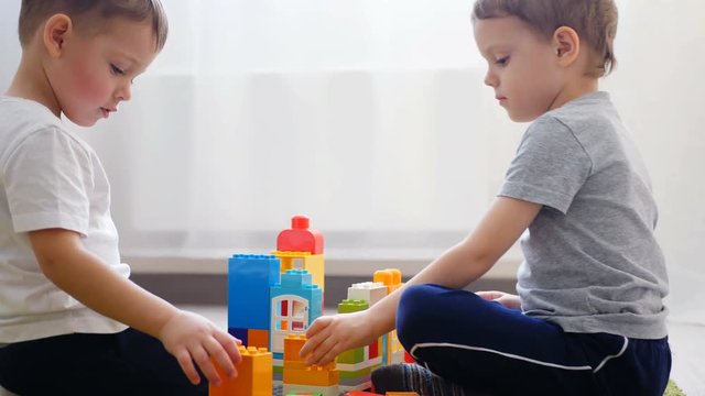 Two little boys are playing with colored blocks on a floor