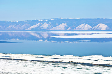 Spring landscape with floating ice floes on blue water and reflection of a mountain range. Siberian lake Baikal