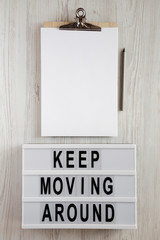 'Keep moving around' words on lightbox, clipboard with sheet of paper and pencil on a white wooden surface, top view. From above, flat lay, overhead.