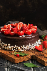 Obraz na płótnie Canvas Cake in chocolate glaze with fresh strawberries on a dark old wood plank background. Selective focus.