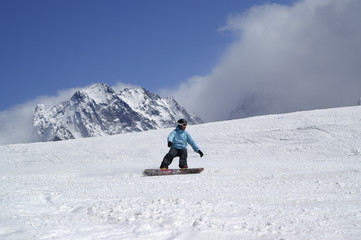 Snowboarder downhill on ski slope in high snowy mountains