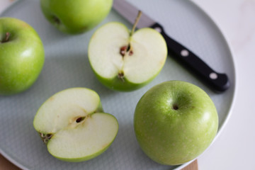 green apples on a gray plate with a knife close up.