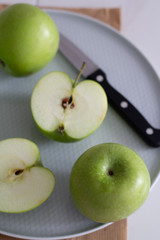 green apples on a plate with a knife top view.
