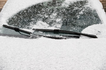 Car wiper blades remove snow from car windows. Snow flakes covered the car in a thick layer....