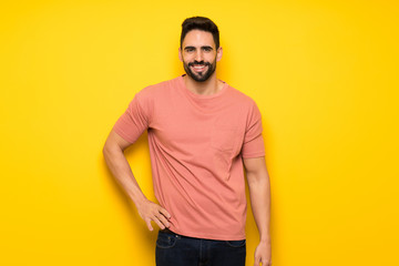 Handsome man over yellow wall posing with arms at hip and smiling