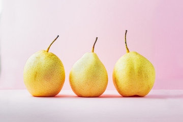 Three fresh yellow pears over pink background