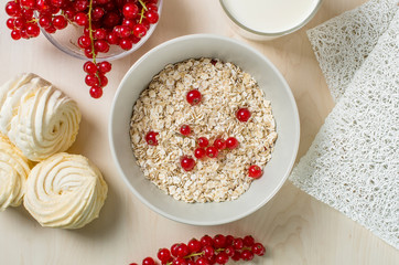 Breakfast served with oatmeal, a glass of milk, cranberry and marshmallow on a wooden background. Flatlay