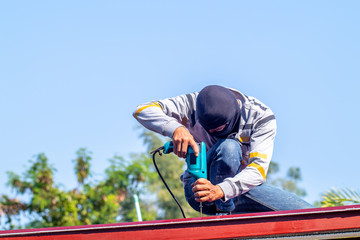 Man is drilling the iron or metal frame for buildinh the roof during house construction with blue sky background.  © guidenuk