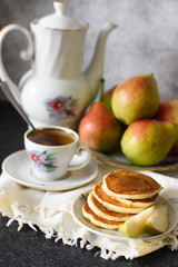 Fresh baked pancakes with pear and tea on the background of a concrete wall