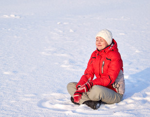 Fototapeta na wymiar Beautiful smiling young girl sitting in the snow in the lotus position and enjoys the flying snow.
