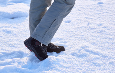 Female legs in winter pants and boots on white snow in a winter sunny day.